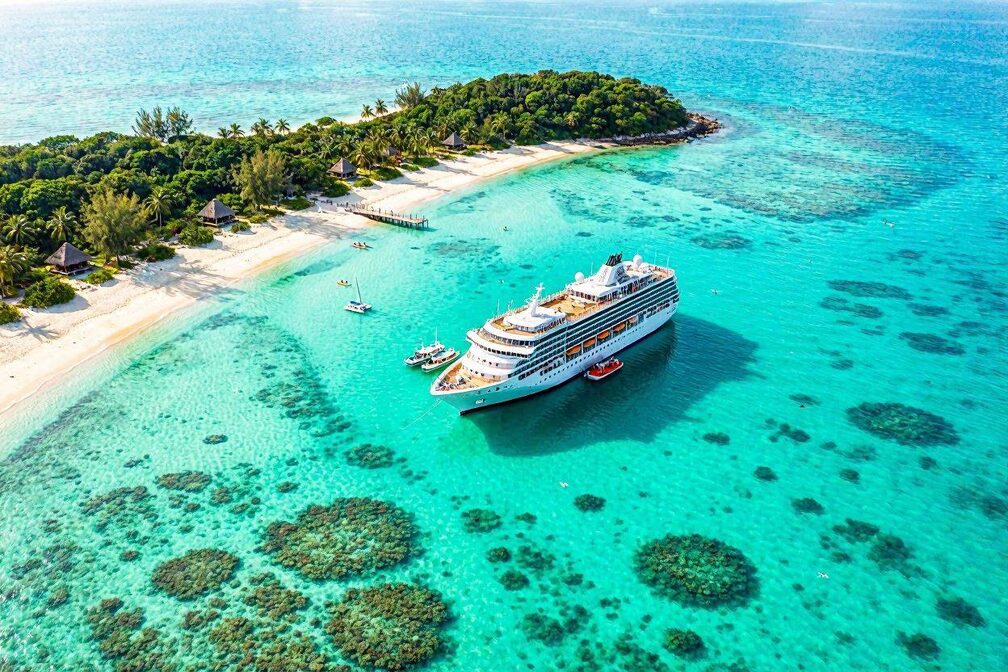 Aerial view of turquoise Caribbean waters with a Norwegian cruise ship anchored near a tropical island, white sandy beaches and vibrant coral reefs visible from above alongside lush green coastline